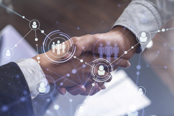 Three coworkers standing around a touchscreen displaying charts and graphs, with one person pointing at the digital dashboard.