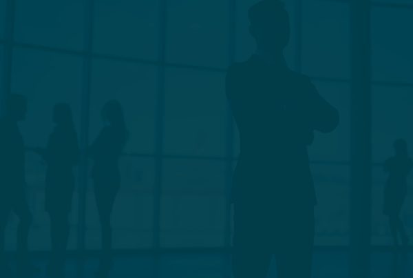 Group of silhouetted professionals engaged in conversation near large office windows during daylight