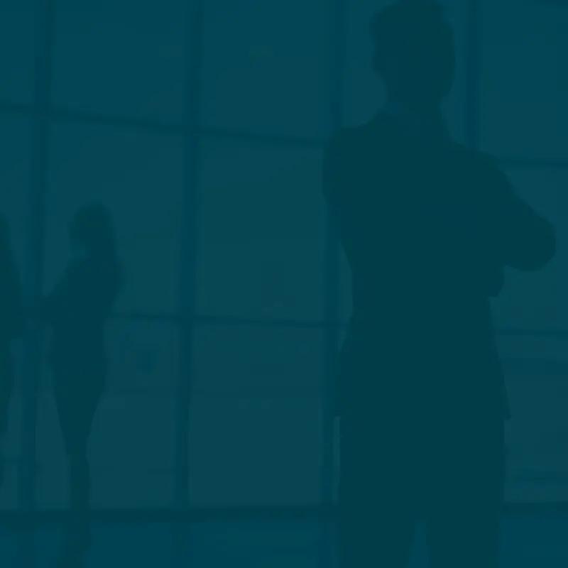 Group of silhouetted professionals engaged in conversation near large office windows during daylight